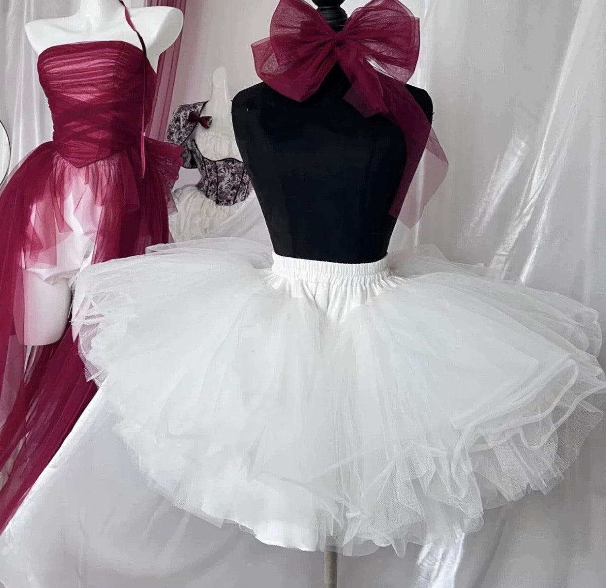 Mannequin wearing a black top with a large pink bow and a white tutu skirt against a white curtain.