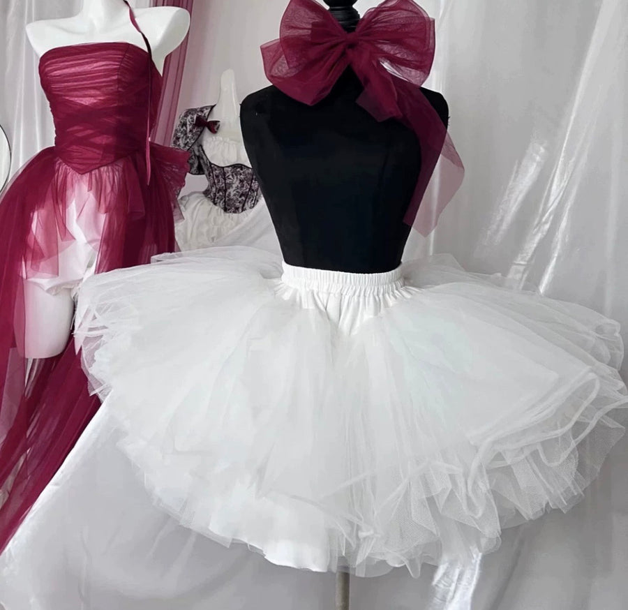 Mannequin wearing a black top with a large pink bow and a white tutu skirt against a white curtain.