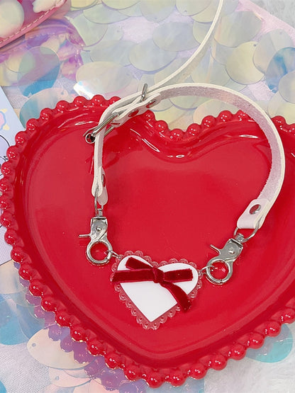 Halsband mit weißem herzförmigem Anhänger und roter Schleife