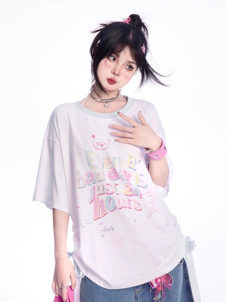 ゆったりとしたTシャツ。裾のディテール。ホワイトのラウンドネック。レタープリント。蝶結び。