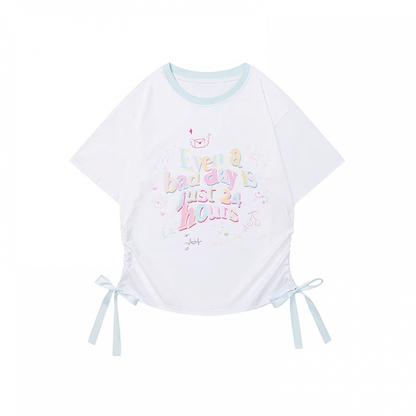 ゆったりとしたTシャツ。裾のディテール。ホワイトのラウンドネック。レタープリント。蝶結び。