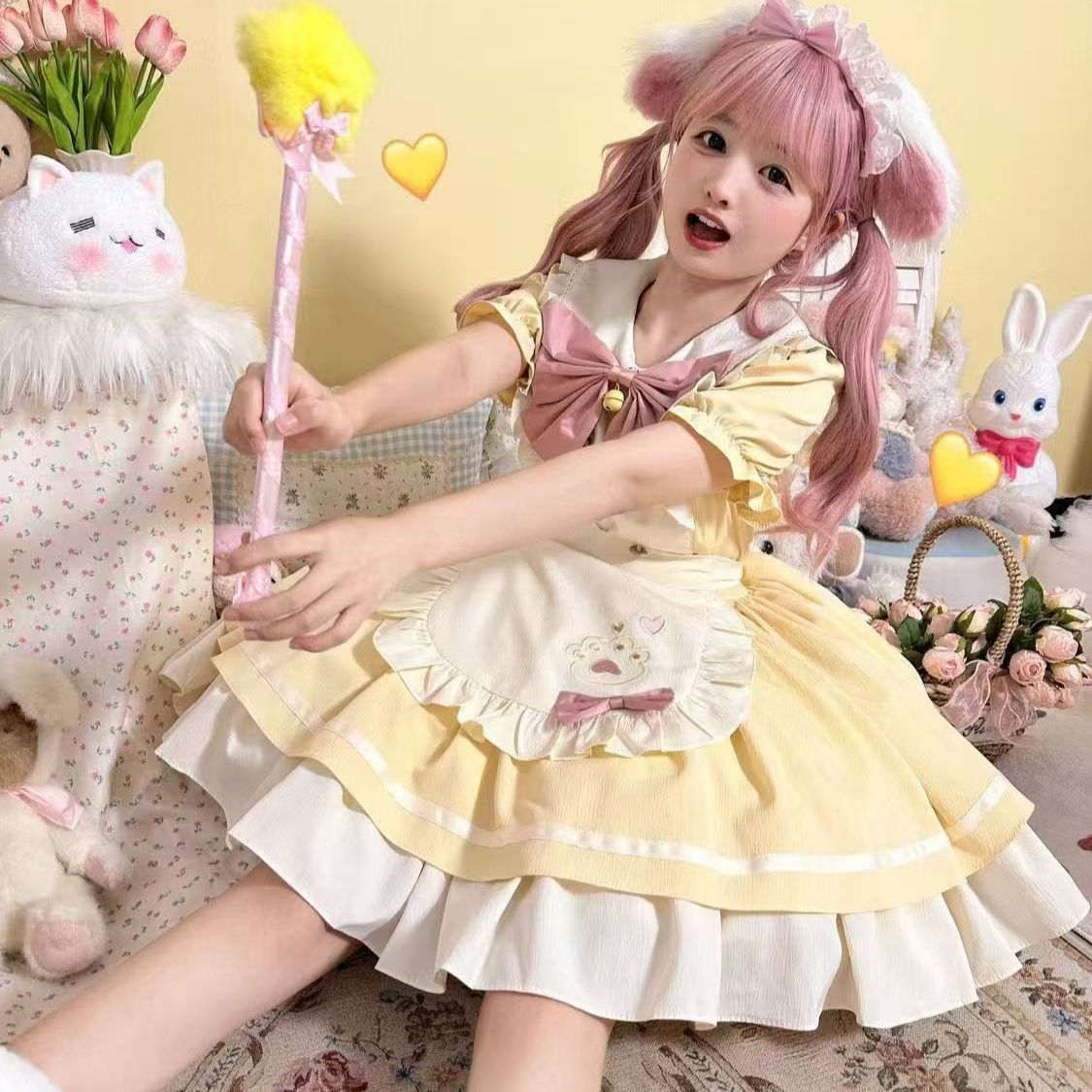 Girl in a yellow and white dress with pink hair, holding a wand, surrounded by plush toys and flowers.